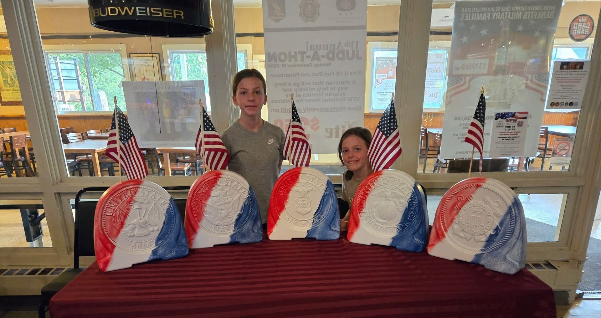Two people standing behind red, white, and blue patriotic display items on a table in a bright lobby