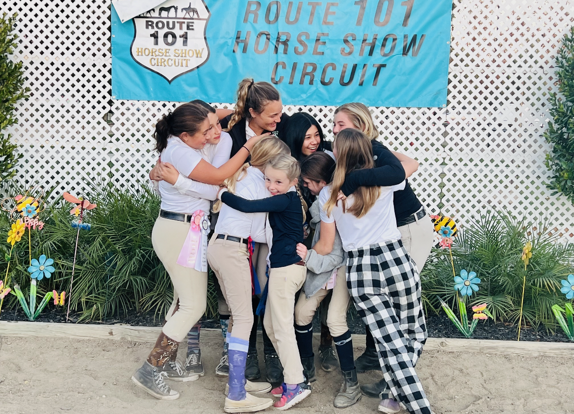 A group of girls hugging in front of a sign that says route 101 horse show circuit
