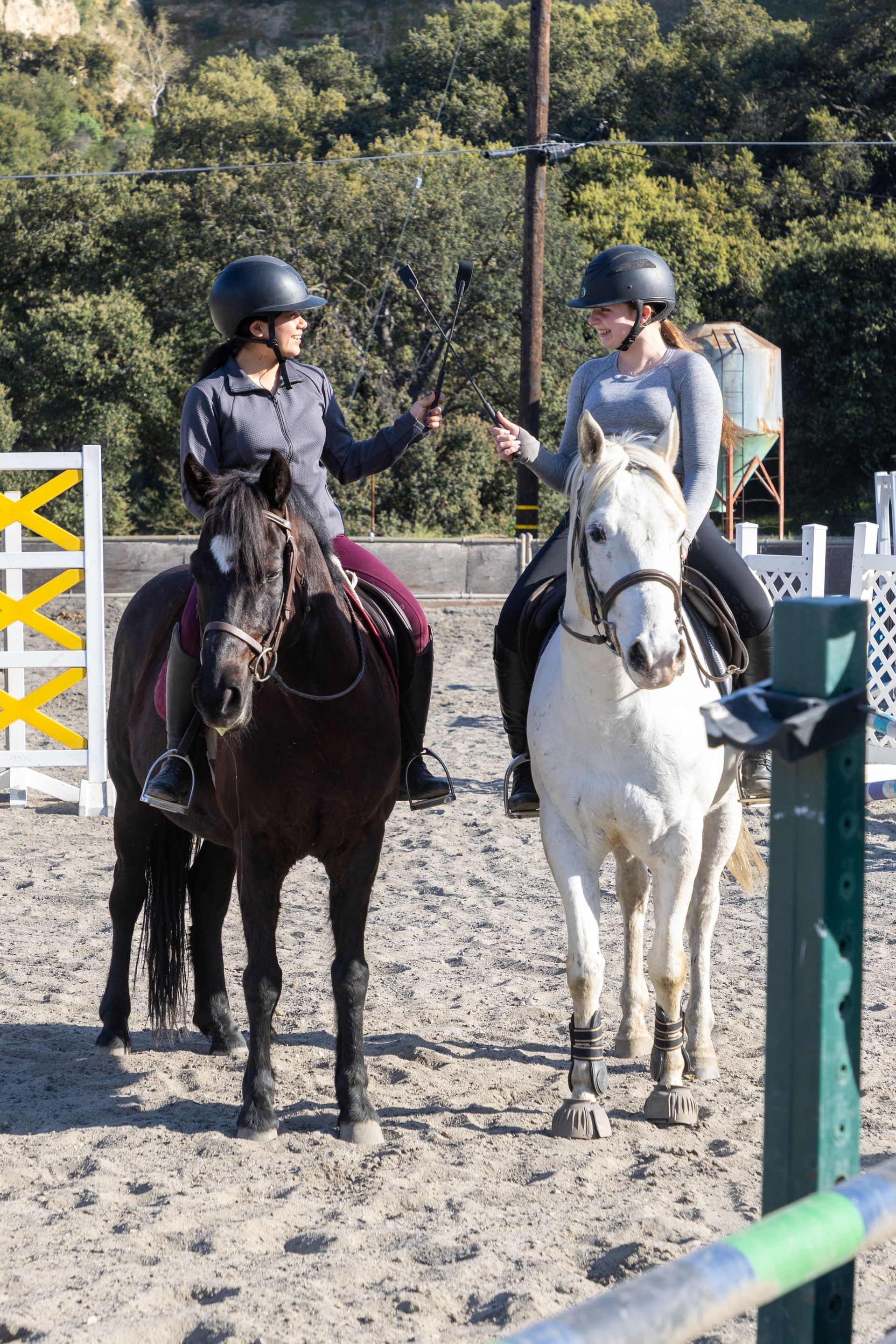 Two women are riding horses in a dirt arena and talking to each other.