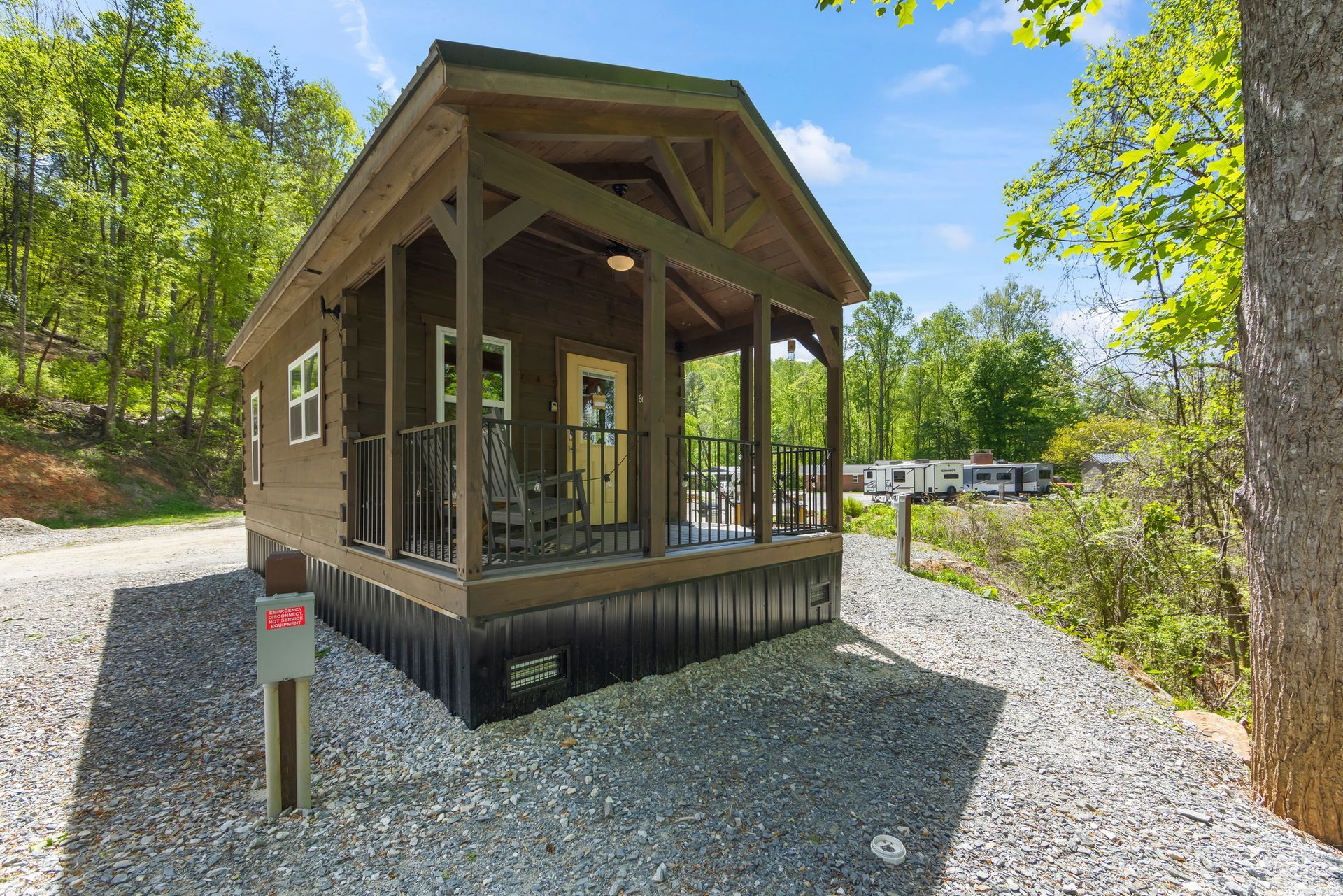 Small rustic cabin with porch in a wooded area beside a gravel path