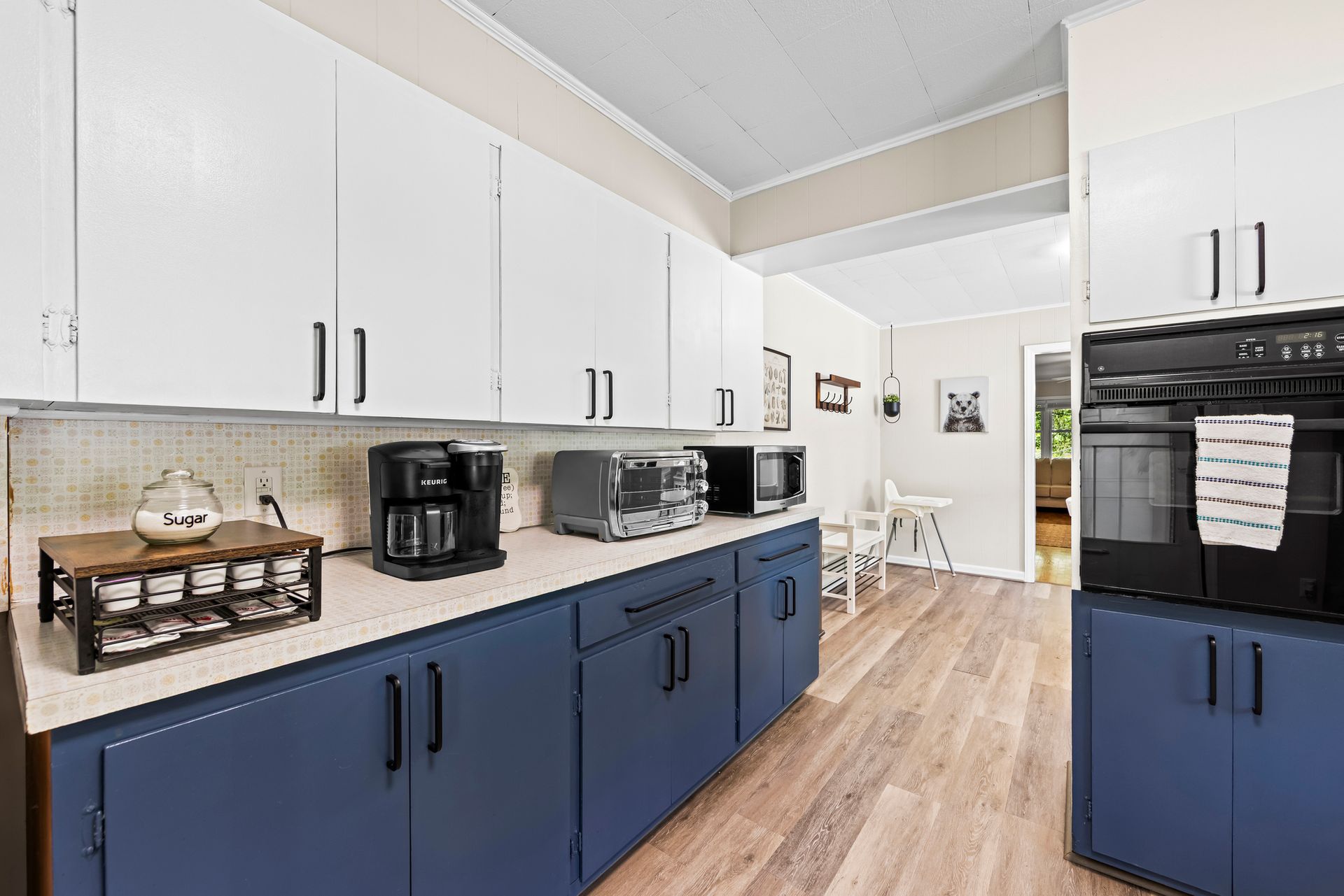 Bright kitchen with white upper cabinets, navy lower cabinets, black appliances, and wood flooring