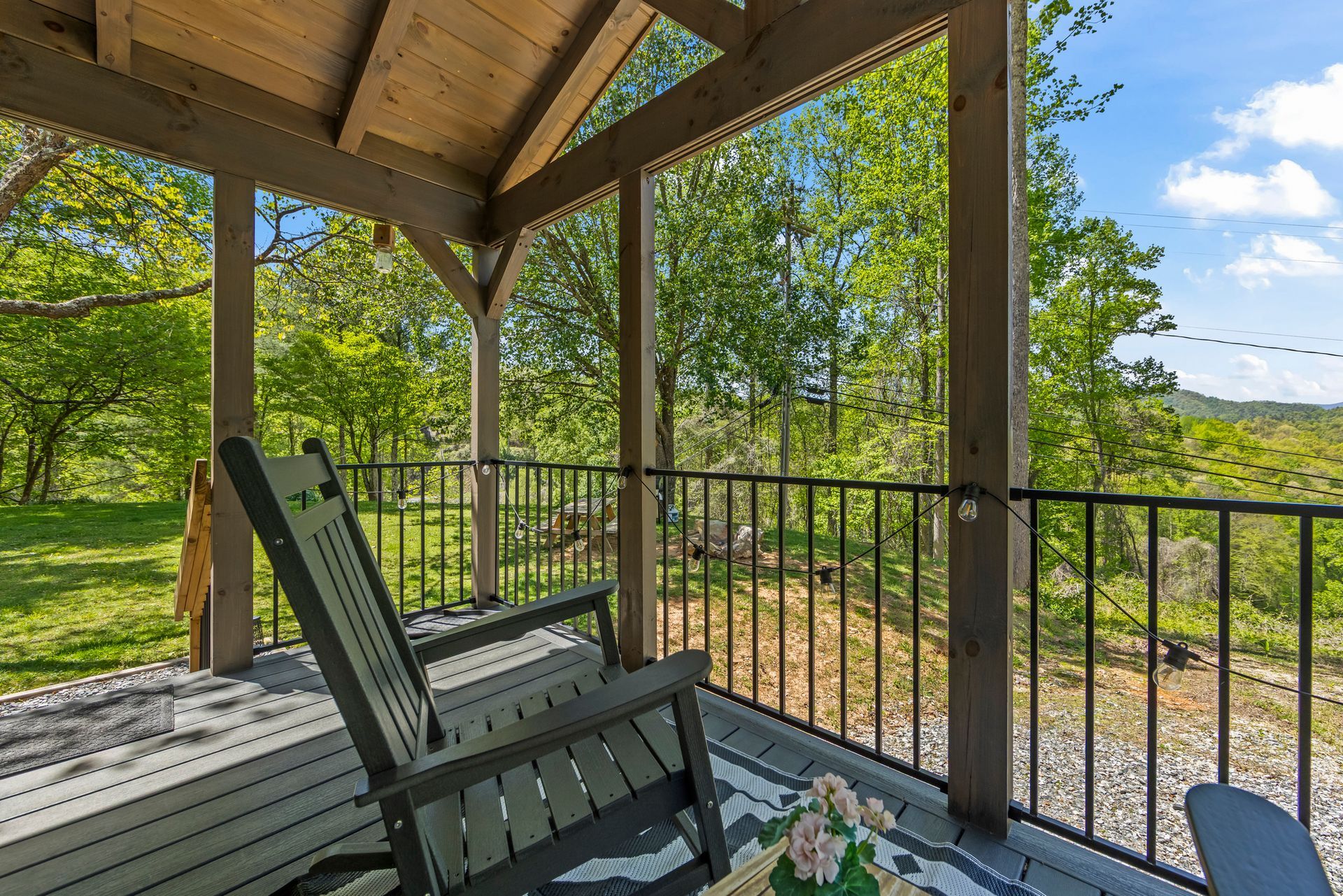 Covered deck with green rocking chair, black railing, and wooded view beyond.
