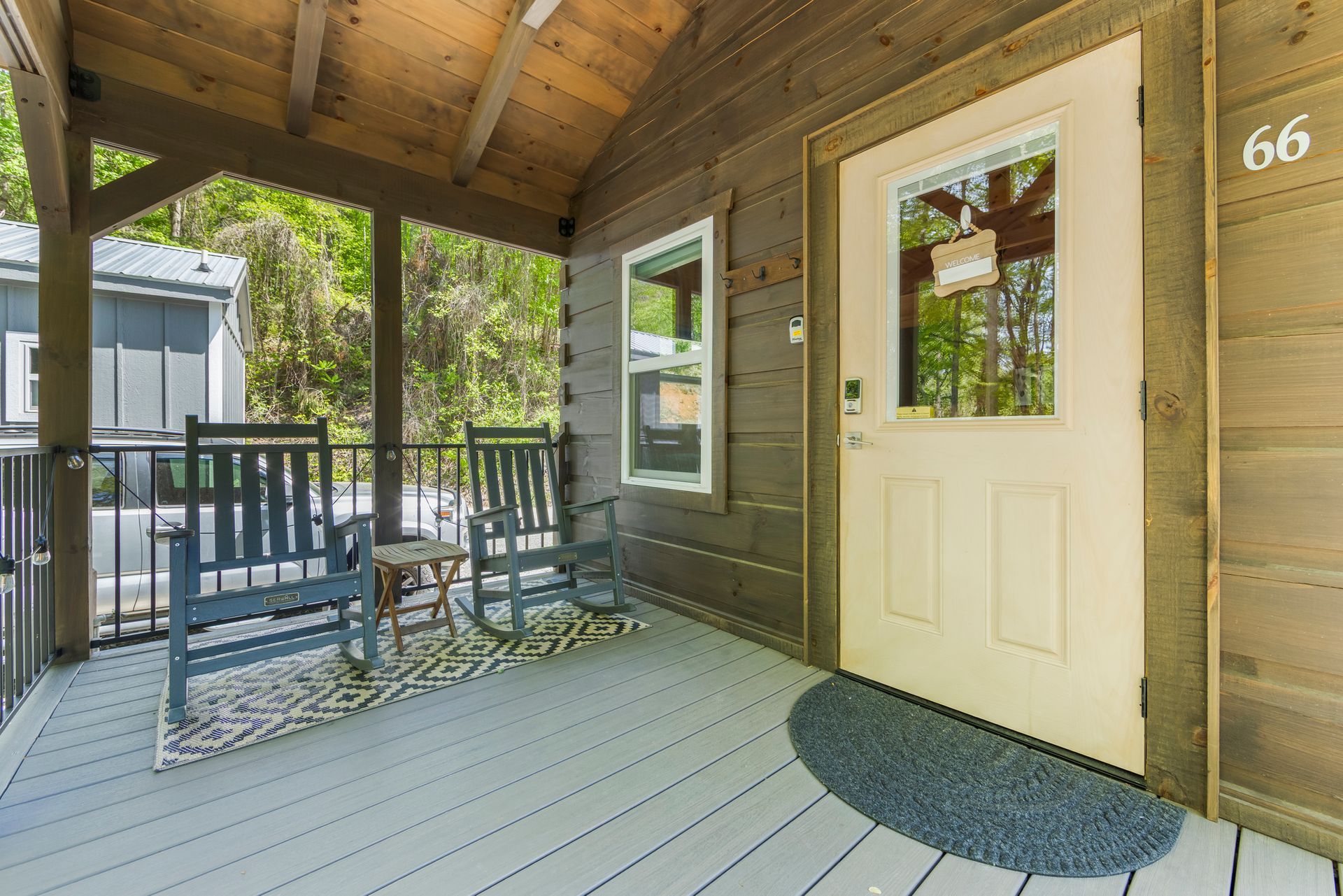 Covered porch with rocking chair, railing, white door, and black doormat outside apartment 66