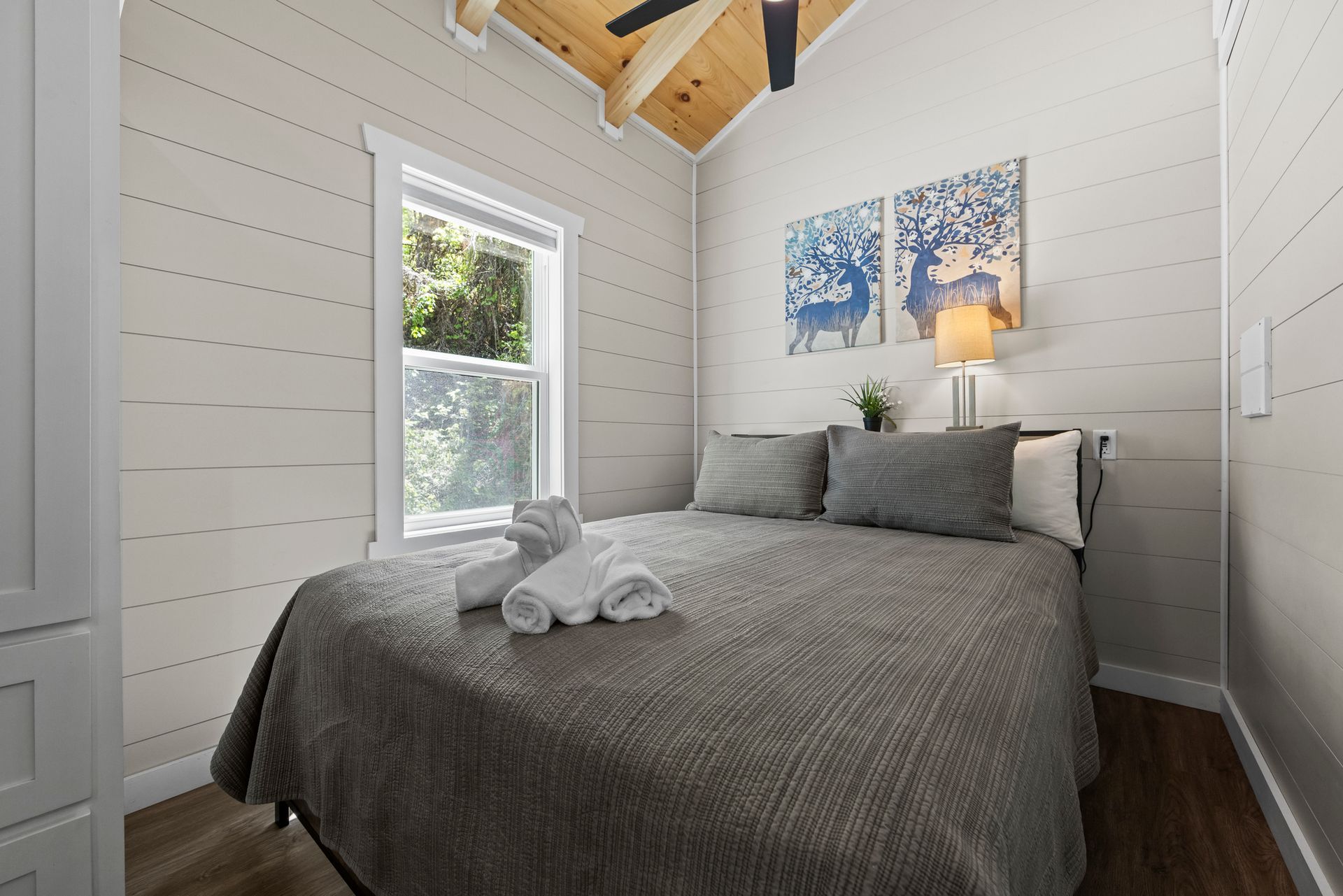 Bright bedroom with gray bedspread, white walls, window, lamp, and blue wall art