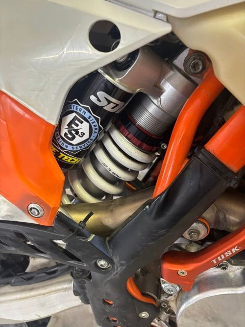 Close-up of a motorcycle rear suspension shock, orange frame, and white bodywork.
