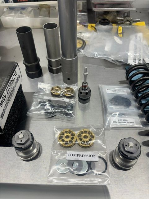 Assorted metal engine parts and springs laid out on a workbench, with labeled plastic bags.