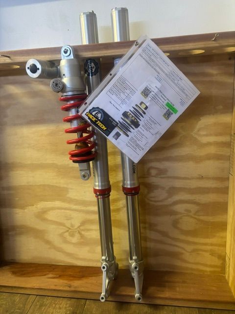 Red motorcycle front forks with red springs and a product tag hanging on a wooden wall display.