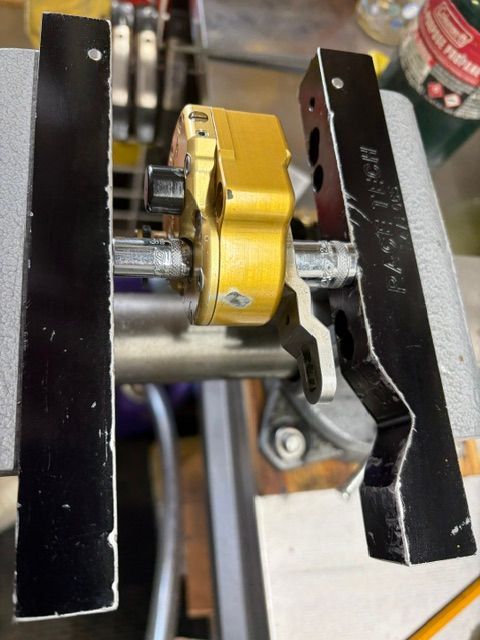 Close-up of a yellow mechanical clamp mounted between two black metal rails with a central shaft.
