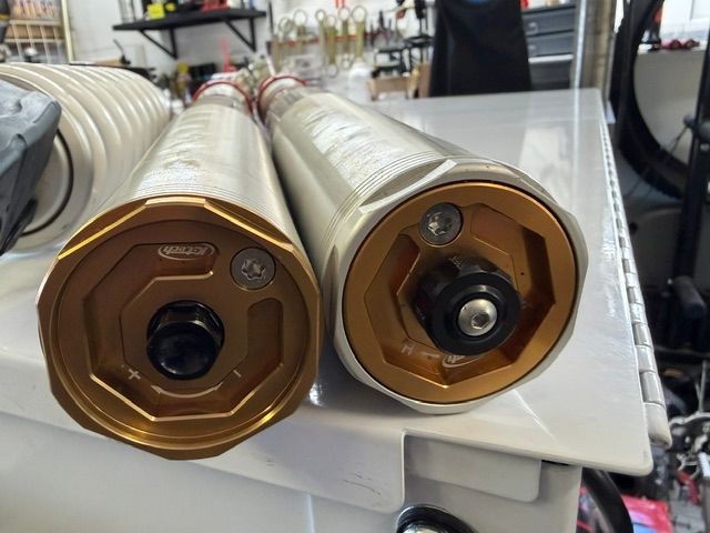 Two gold cylindrical rollers with hexagonal end caps on a white machine table.