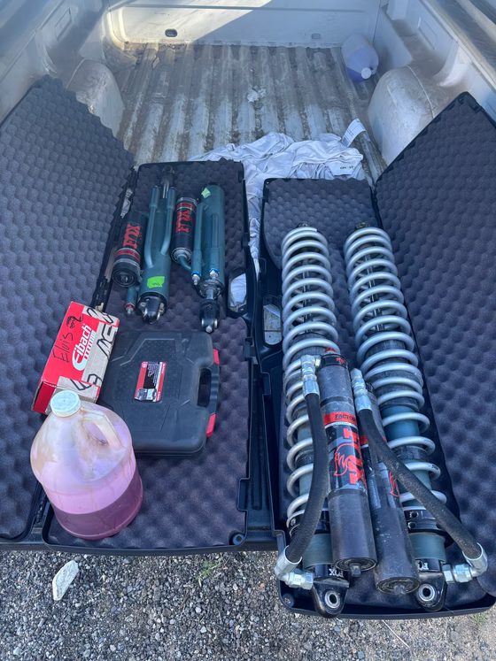 Car trunk with tools and auto parts, including two coil springs, a bottle of fluid, and a toolbox.