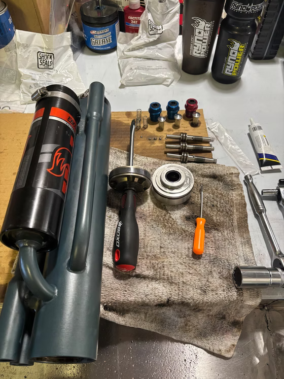 Assorted metal tools and parts laid out on a workbench, including a flashlight and spray canister.