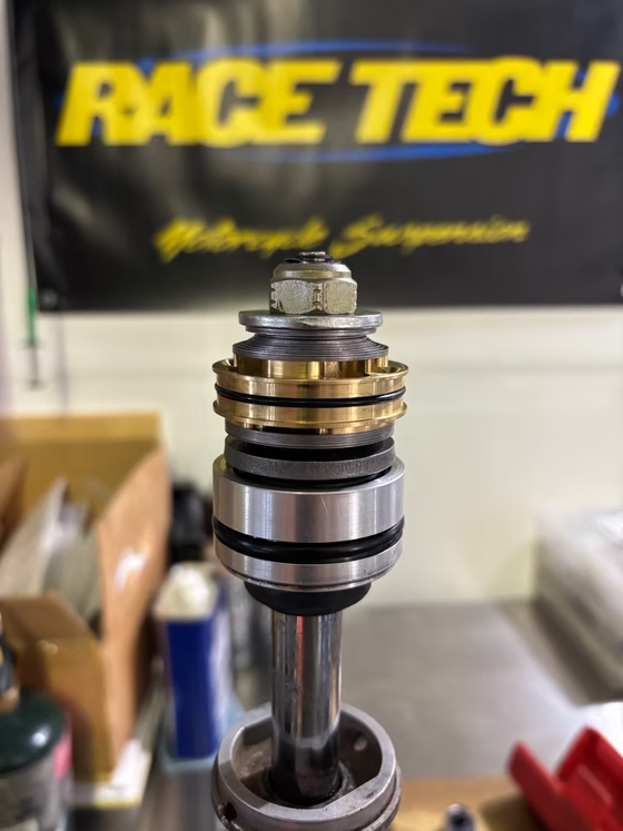 Suspension strut assembly with polished metal piston in front of a Race Tech banner