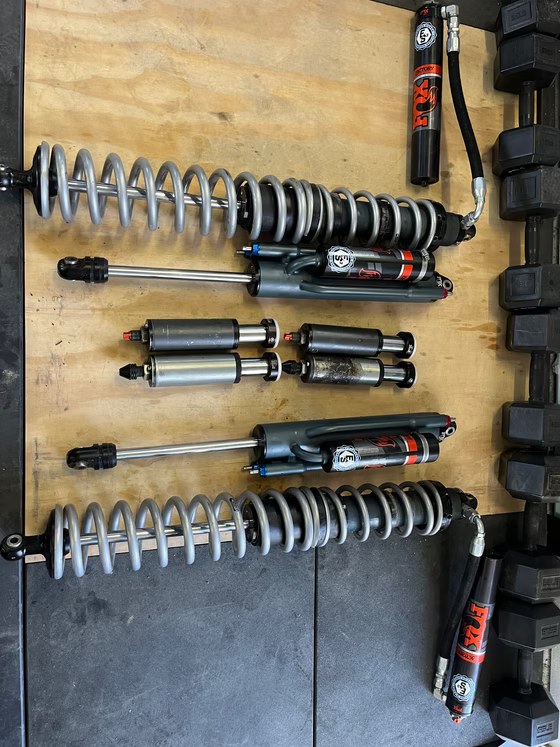 Four motorcycle shocks and coilover suspension parts laid out on a workbench.