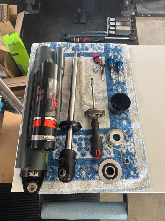 Assorted metal tools and parts arranged on a workbench, including a black cylinder and wrenches.