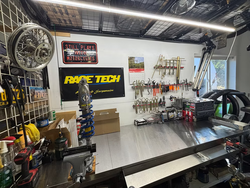 Race Tech motorcycle workshop with tools, parts, and a workbench under bright overhead lights