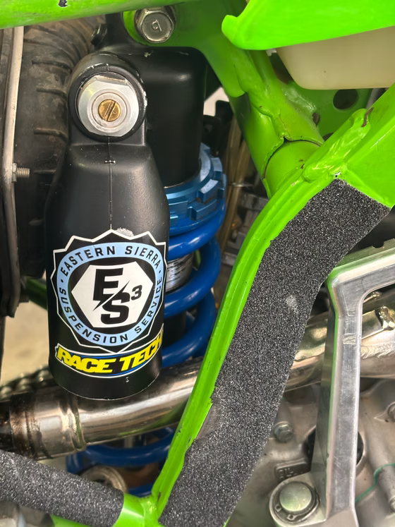 Blue motorcycle shock absorber with ES logo and black frame components in a green bike frame.