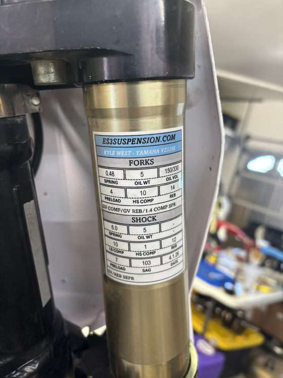Close-up of a bicycle fork with a suspension settings sticker on a gold tube.