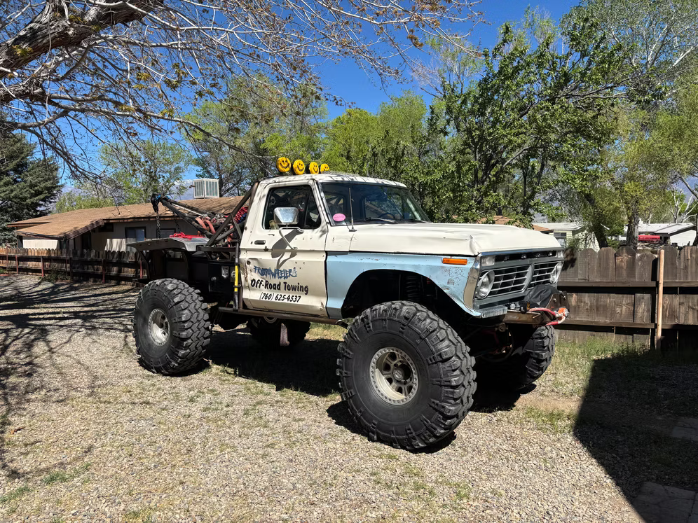 Lifted white off-road pickup with oversized tires parked in a yard under trees