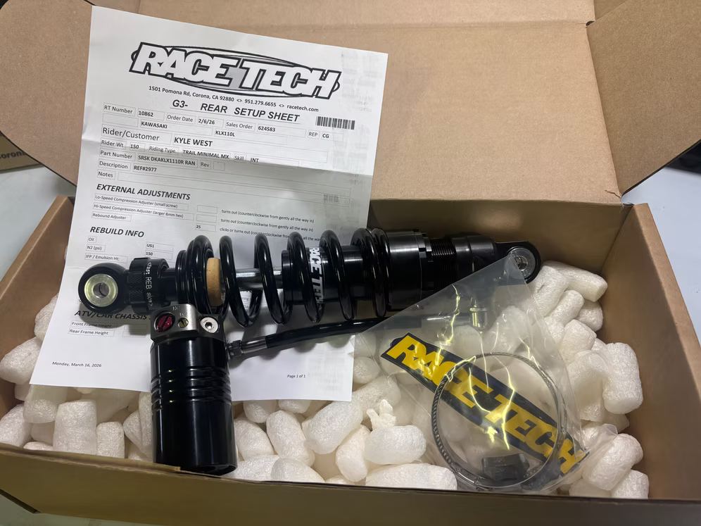 Open box with a black shock absorber, hardware, packing foam, and an instruction sheet.
