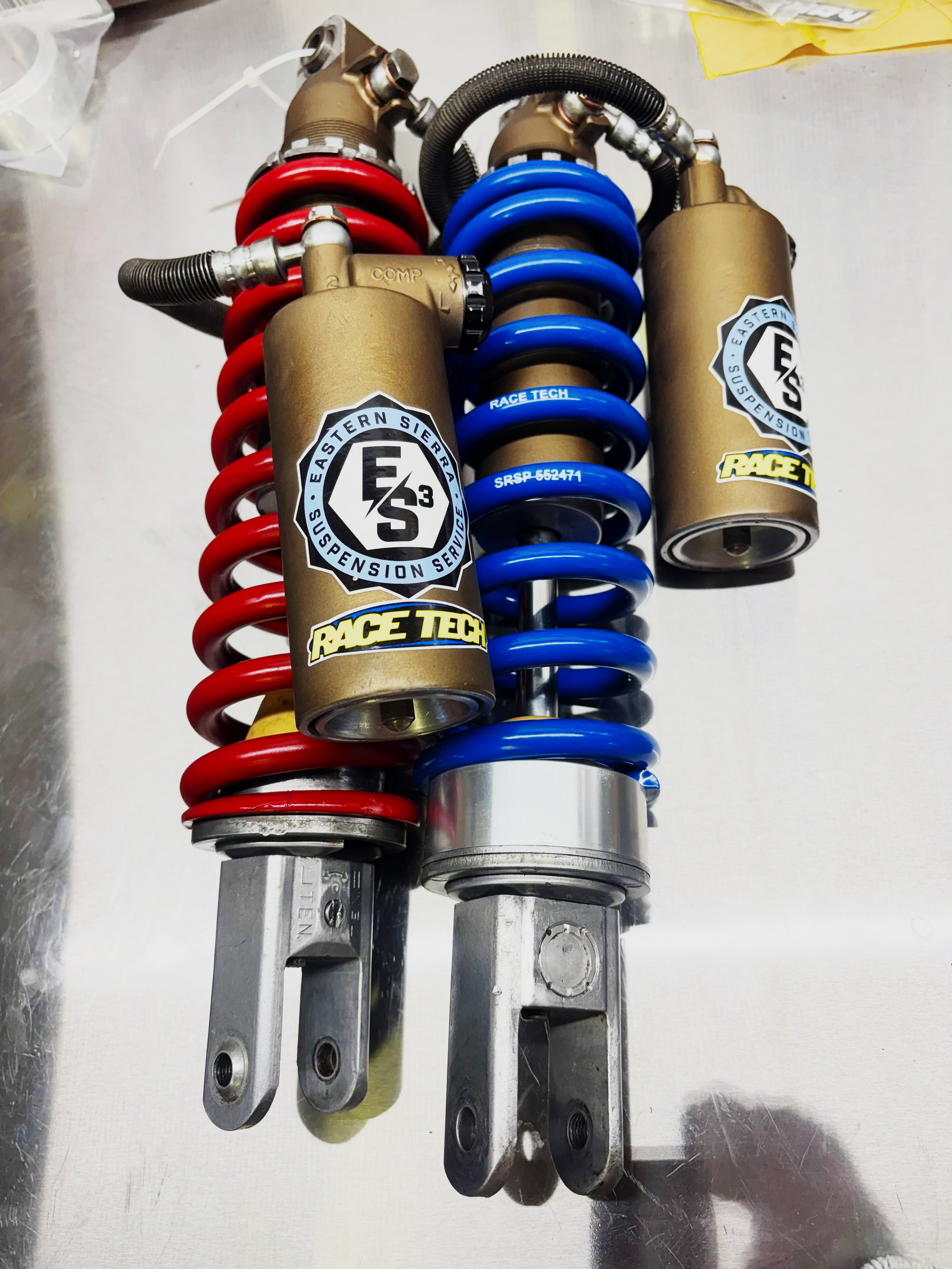 Three coiled motorcycle shock absorbers in red, blue, and tan, arranged side by side.