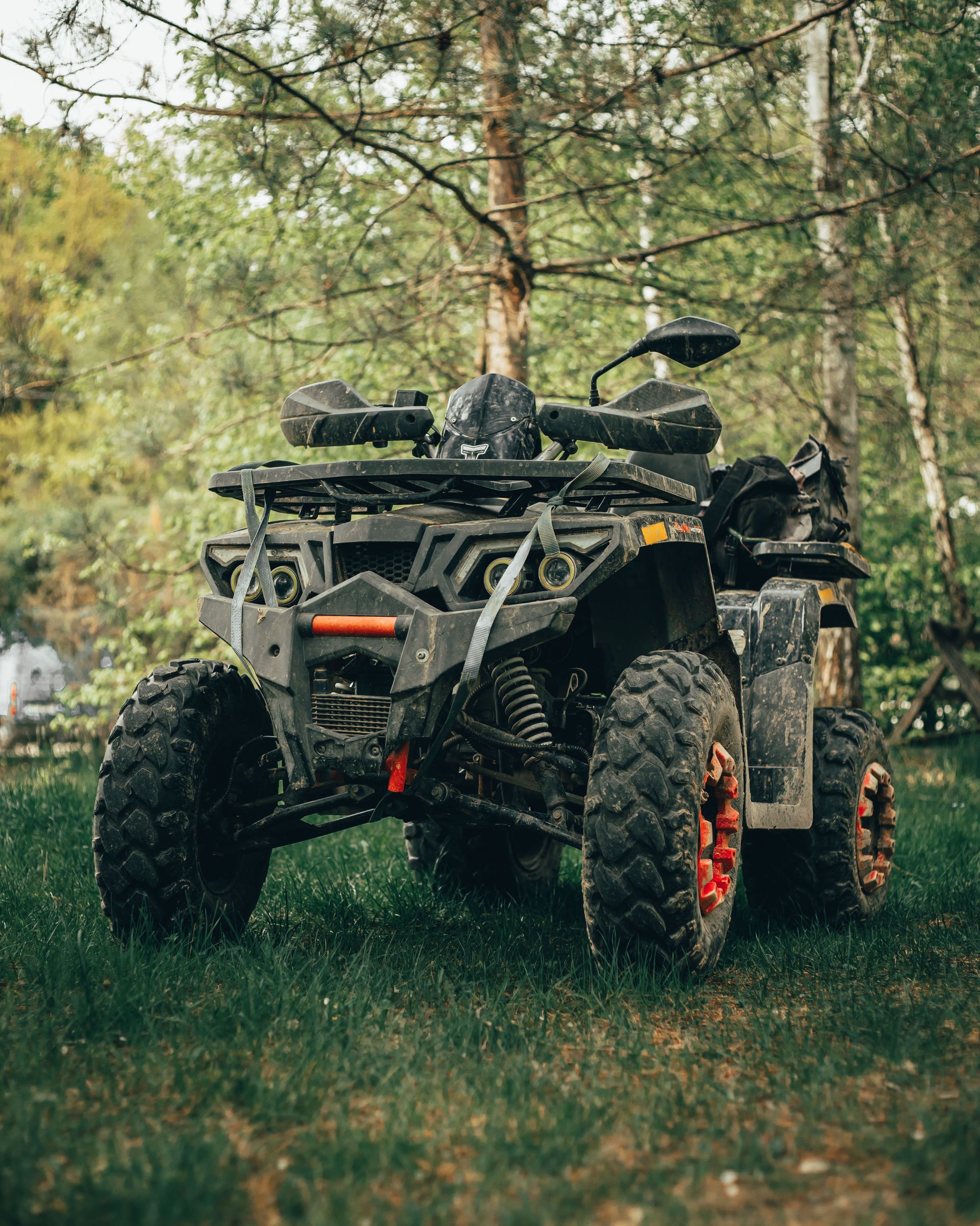 Camouflaged ATV parked in a grassy forest clearing, rear view, with red wheel rims.