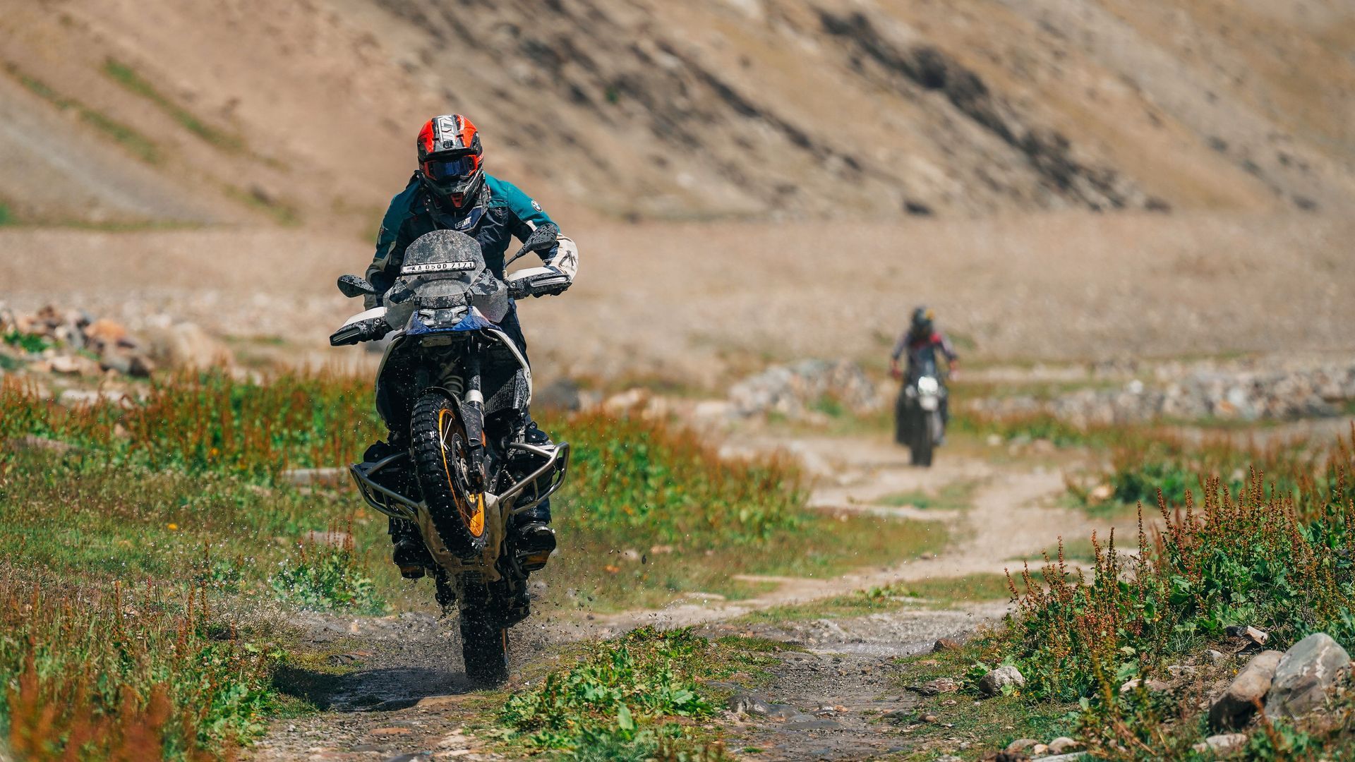 Two dirt bikers ride along a rocky trail, with one speeding toward the camera in the foreground.