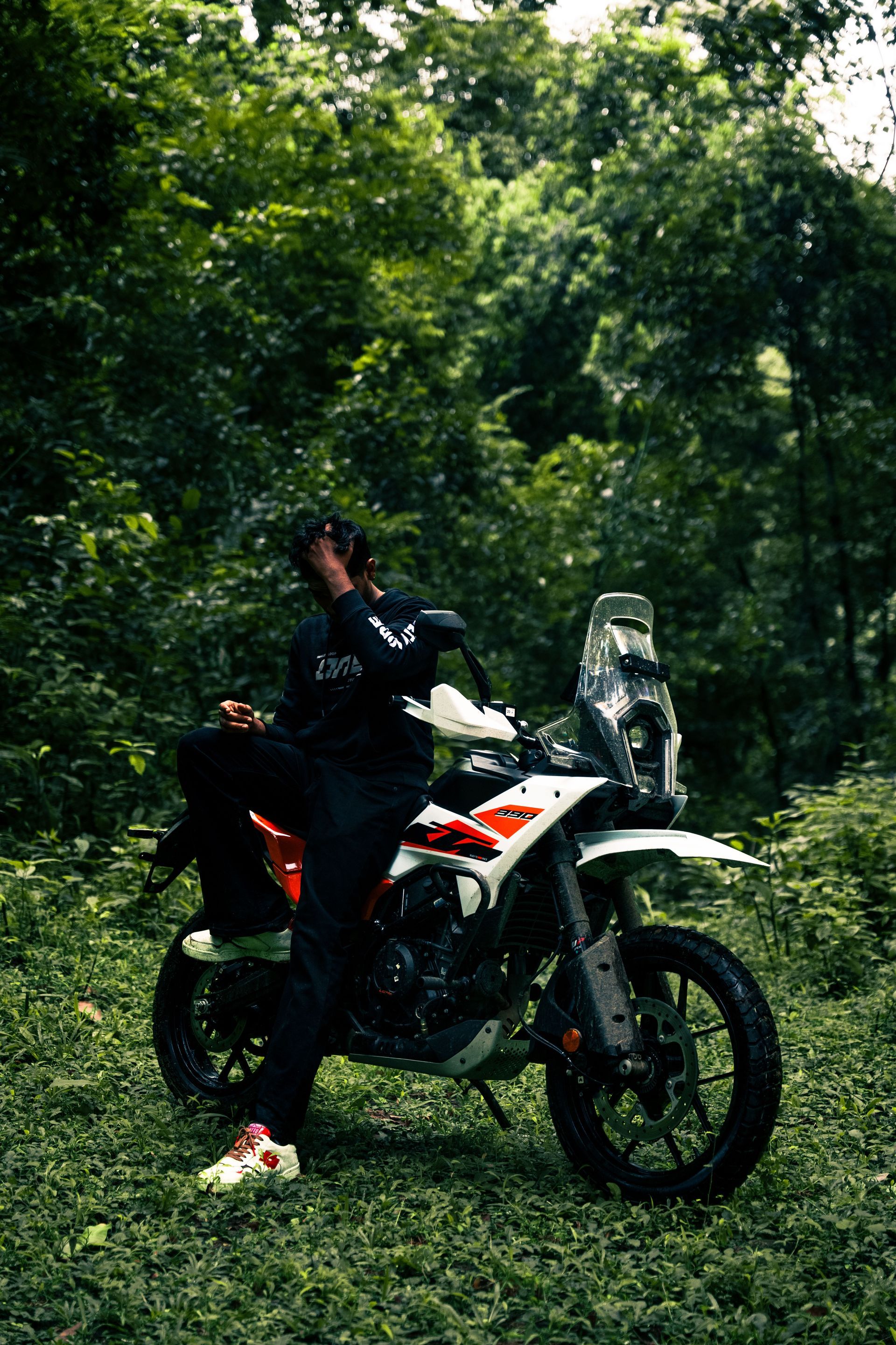Person standing beside a white dirt bike in a green forest clearing.