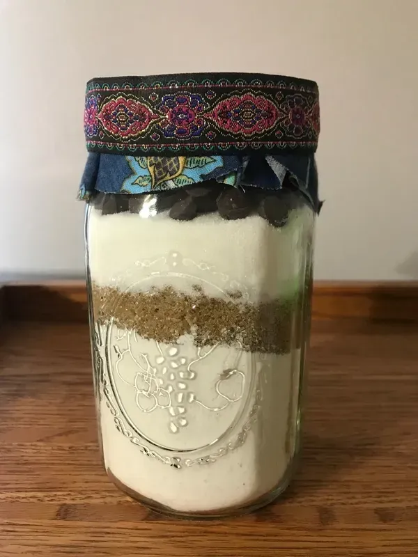 A jar filled with a cookie mix is sitting on a wooden table.