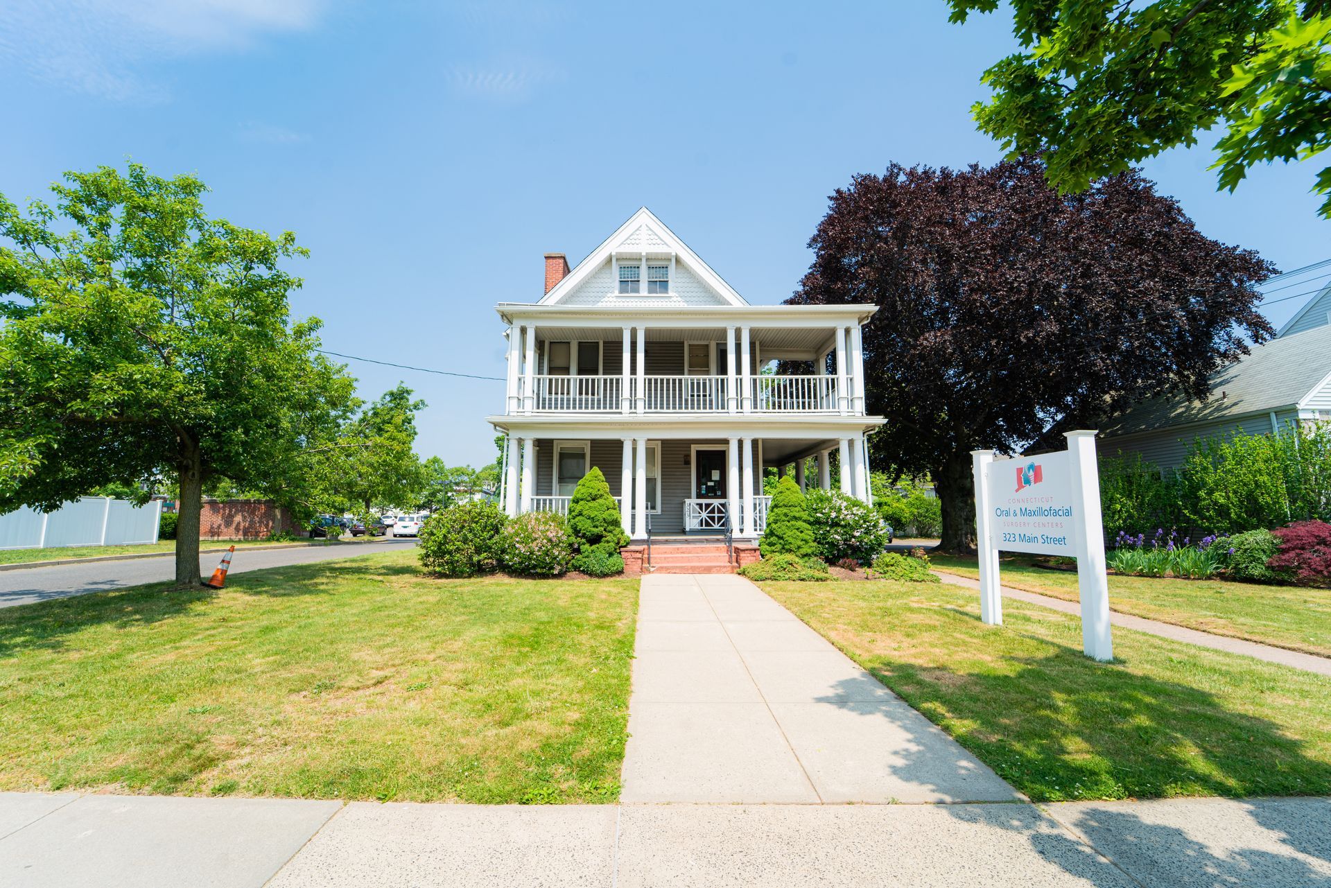 A two-story white house with a double-decker porch and a walkway leading to the front entrance on a sunny day.