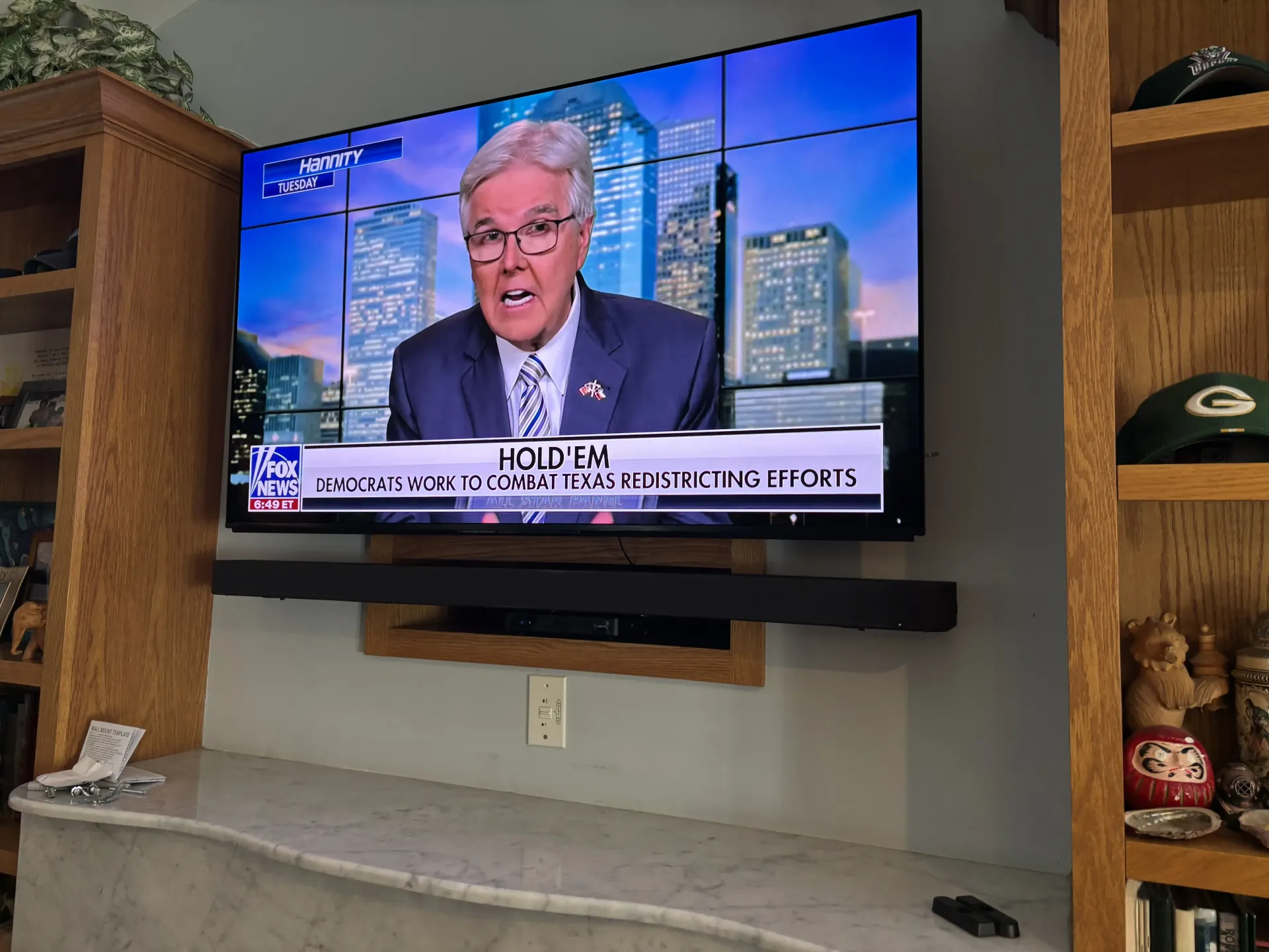 A flat-screen TV mounted above a fireplace mantel displays a news broadcast featuring a man in a suit.