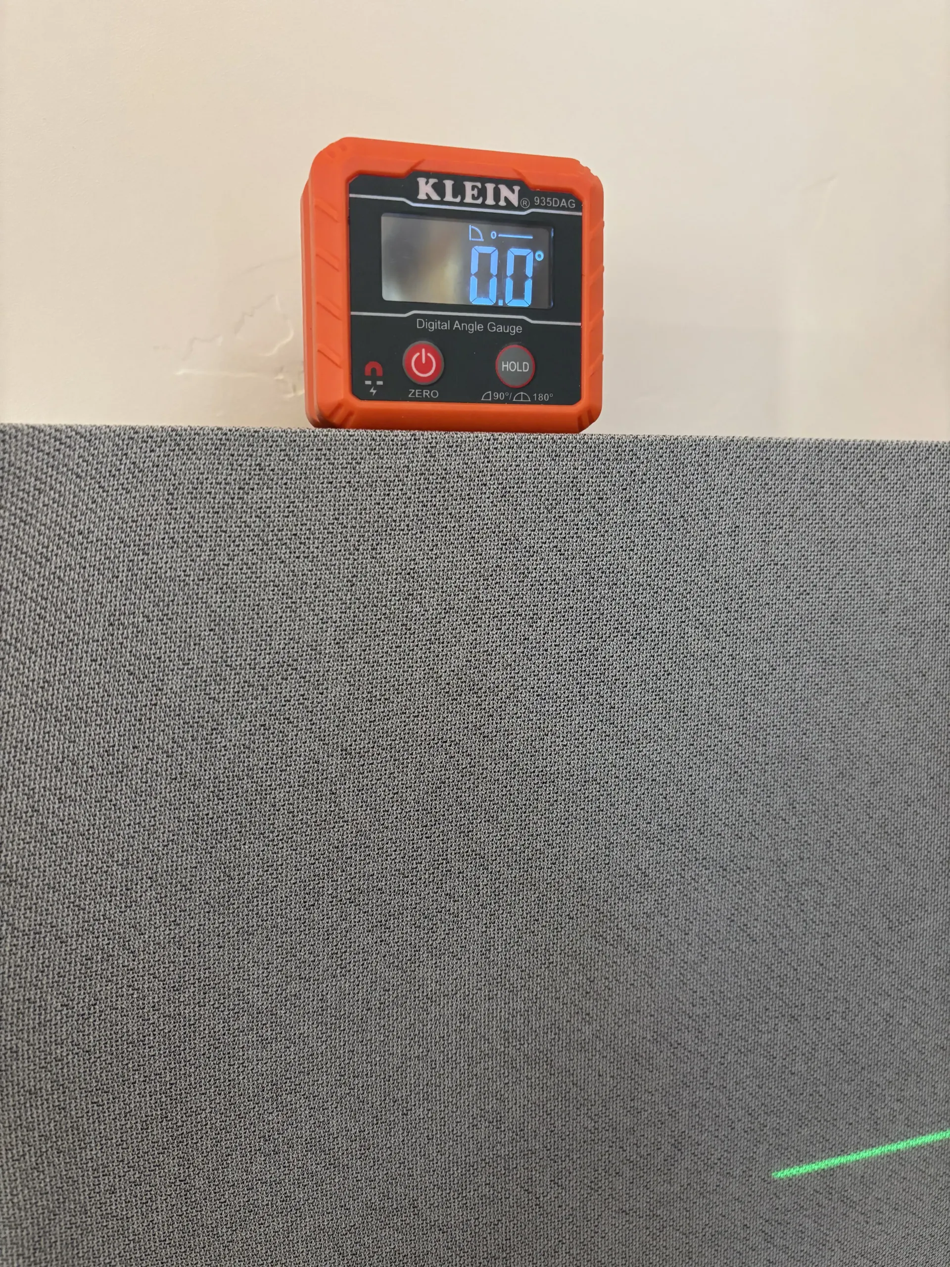 A digital level with an orange case showing 0.0 degrees rests on a textured gray, patterned surface.