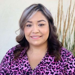 Woman smiling in a pink leopard-print top against a light wall with decorative grasses