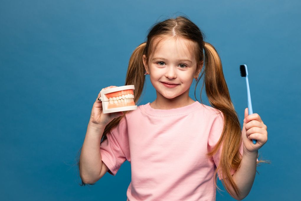 Smiling child holding toothpaste and a toothbrush against a blue background