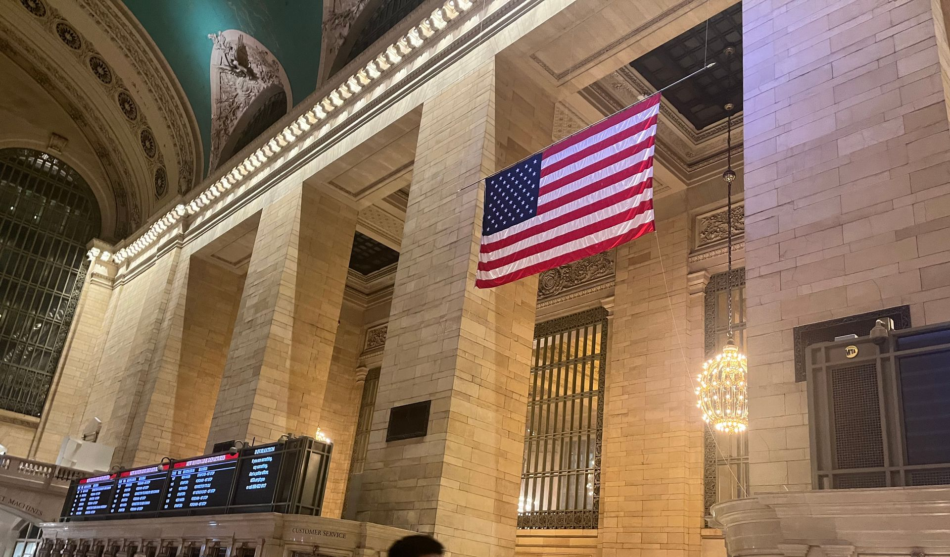 Amerikansk flag hænger i Grand Central Terminal, NYC, ved siden af ​​afgangstavler.