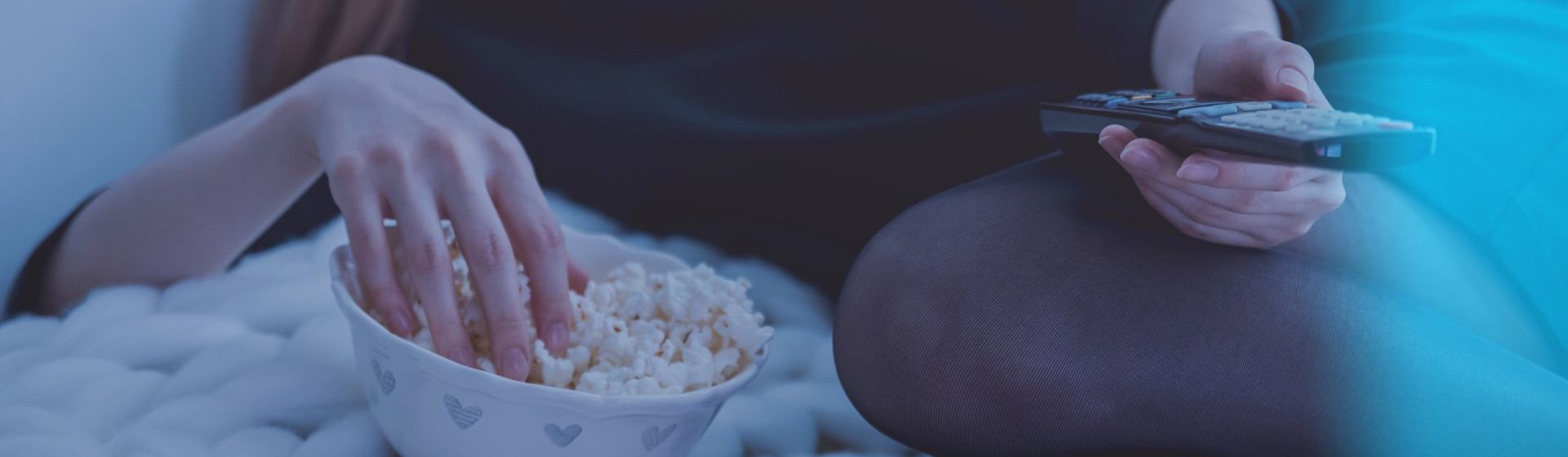 En kvinde sidder på en sofa og spiser popcorn og holder en fjernbetjening.