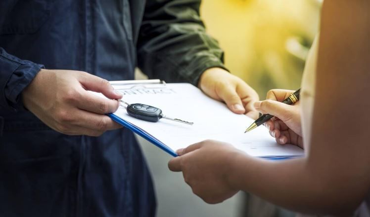 Intercambio de manos entre un portapapeles y las llaves del coche durante una firma o transacción.