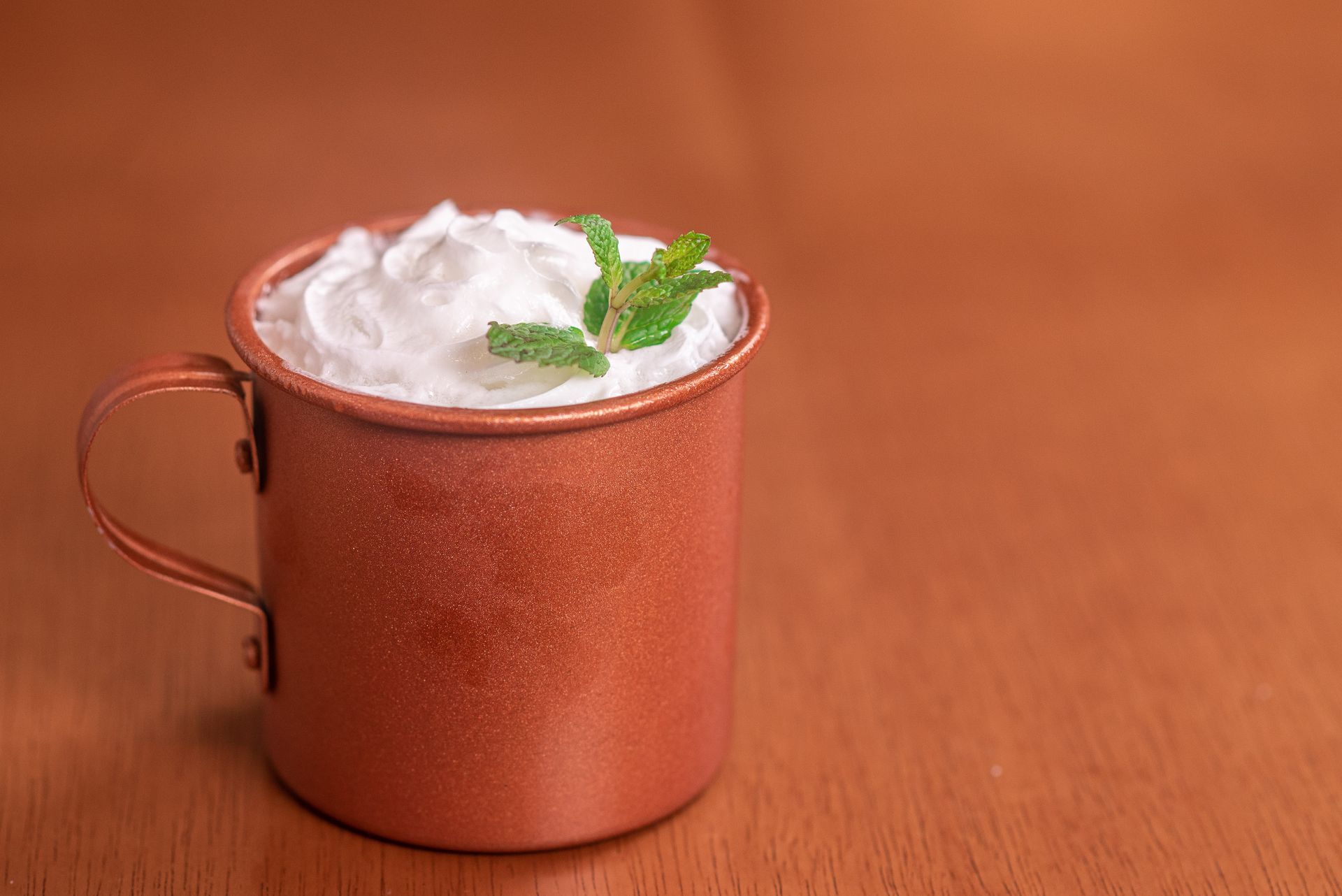 A cup of whipped cream with mint leaves on a wooden table.