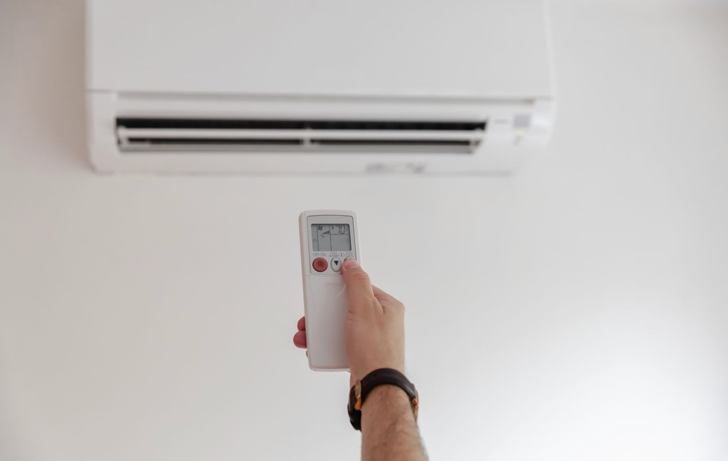 A Person is Holding a Remote Control in Front of an Air Conditioner - DMC Electrical & Air Cooling Pty Ltd in Ayr, QLD