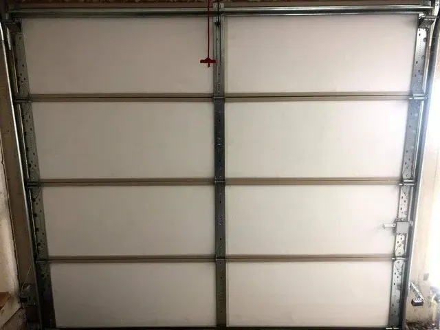 An interior view of a white, multi-panel sectional garage door with metal vertical supports and tracks.