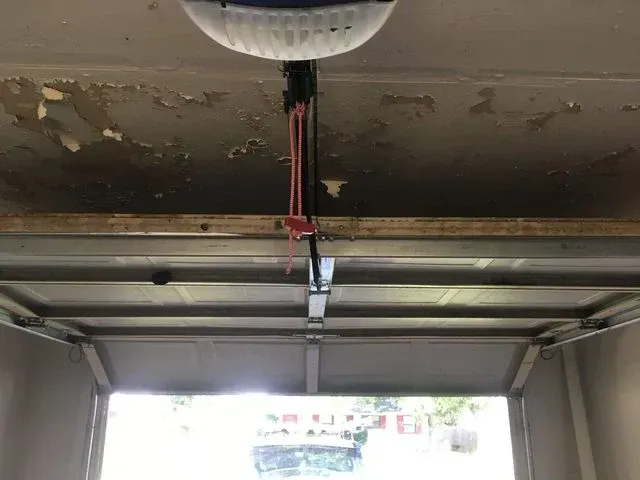 A garage door opener is mounted to the ceiling, with a red manual release cord hanging down above the garage door.