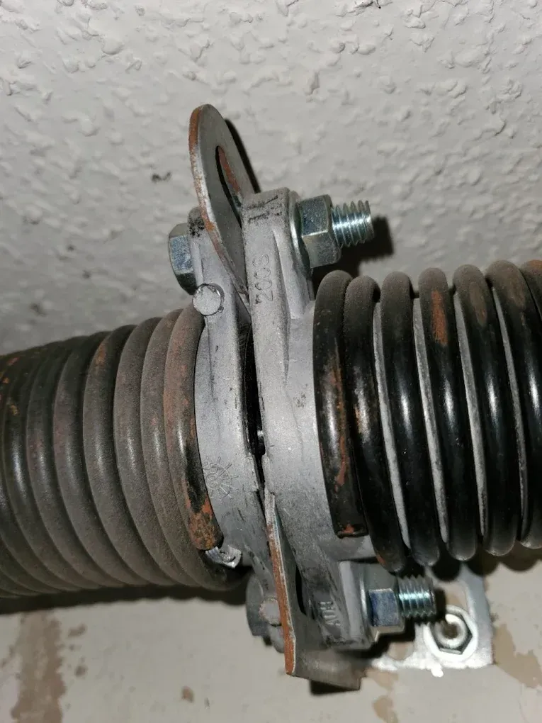 A close-up view of a metal garage door torsion spring showing a cracked, broken stationary cone bracket.