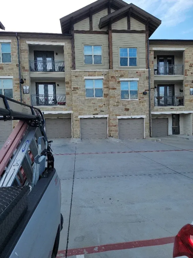 A multi-story apartment building with stone siding and balconies, viewed from a parking lot with a truck in the foreground.