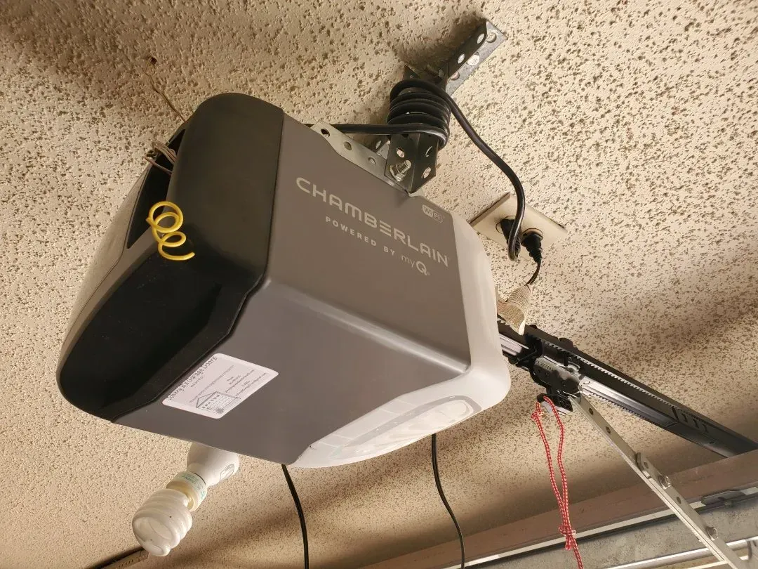 A Chamberlain garage door opener mounted to a ceiling with a power cord plugged into an outlet.