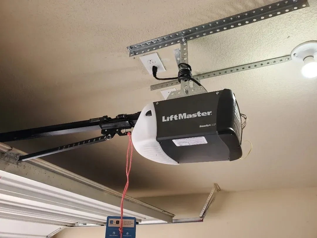 A LiftMaster garage door opener mounted to a ceiling with a hanging red emergency release cord.
