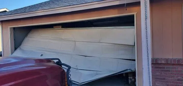 A cream-colored garage door is collapsed and buckled inward toward the inside of the garage.