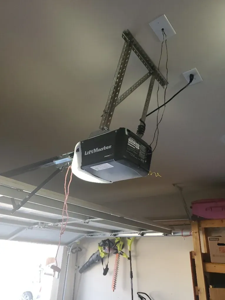 A LiftMaster garage door opener mounted to a ceiling with metal brackets, featuring a hanging red emergency pull cord.