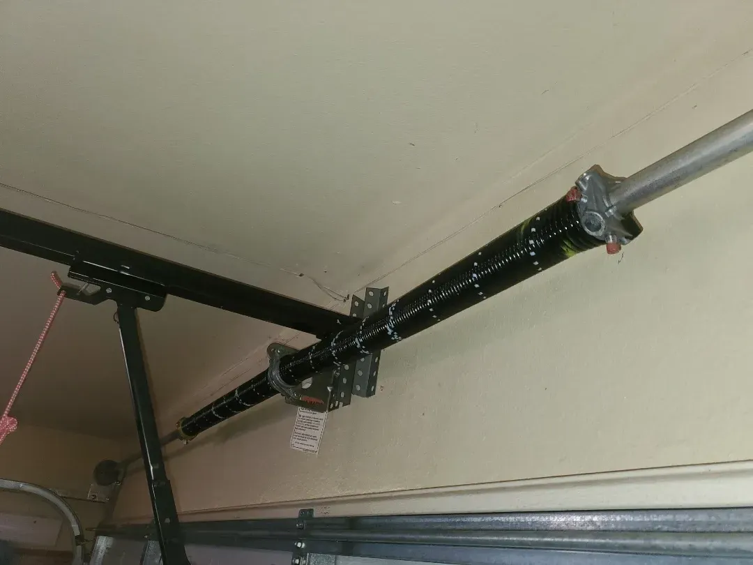 A black horizontal torsion spring assembly mounted above a residential garage door.