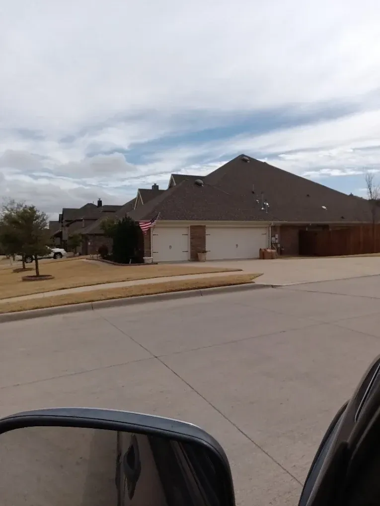 A residential street view of suburban houses with brown roofs and garage doors under a cloudy sky.