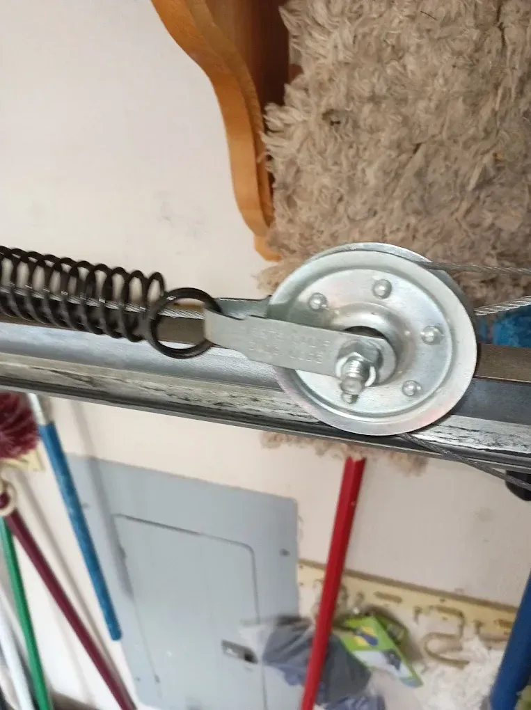 A metal garage door spring attached to a pulley assembly on a horizontal track.