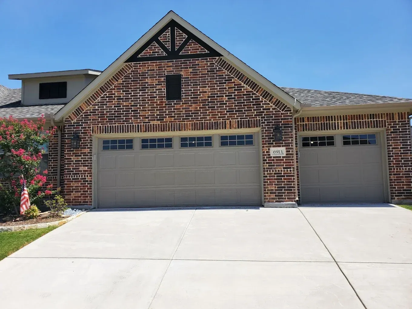 A suburban house with a multi-colored brick facade, a two-car garage, a concrete driveway, and a clear blue sky.